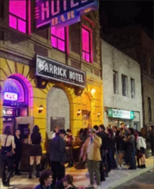Line outside the Garrick Hotel on Garry Street at night, neon sign lit pink