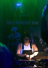 DJ playing under green lasers in front of a Live at the Garrick Hotel sign